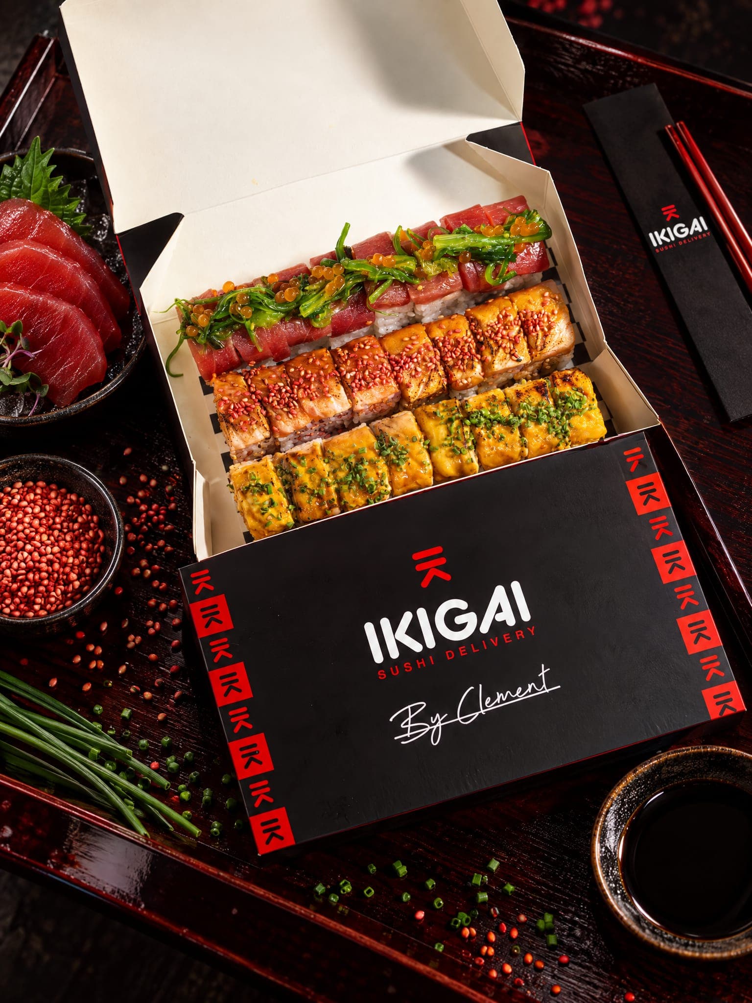 Caja de Ikigai abierta con tres filas de piezas de sushi, sobre una bandeja oscura con palillos